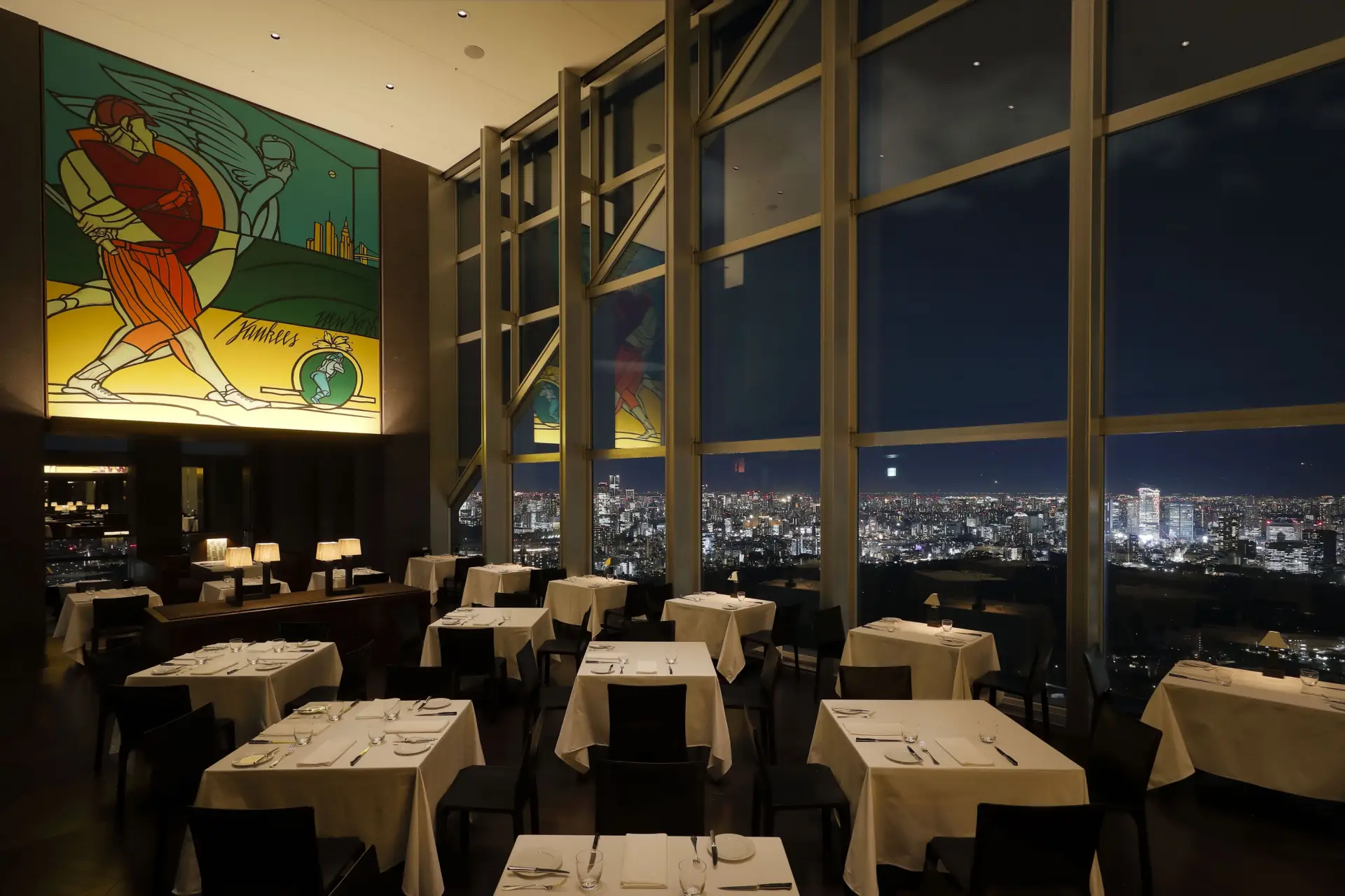 Interior of New York Grill at Park Hyatt Tokyo with floor-to-ceiling windows overlooking the city skyline at night.