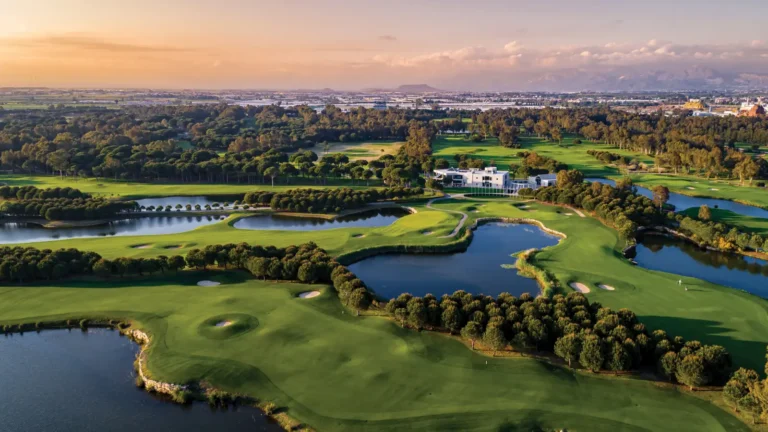 Aerial view of Antalya Golf Club showing green fairways, water hazards and clubhouse surrounded by trees