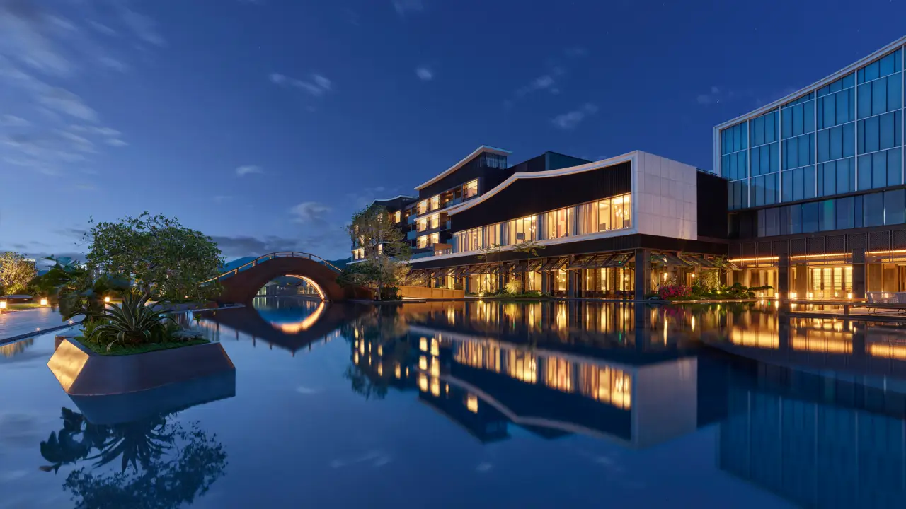 Night view of Banyan Tree Zhuhai Phoenix Bay with illuminated buildings reflected in calm waterfront and an arched bridge.