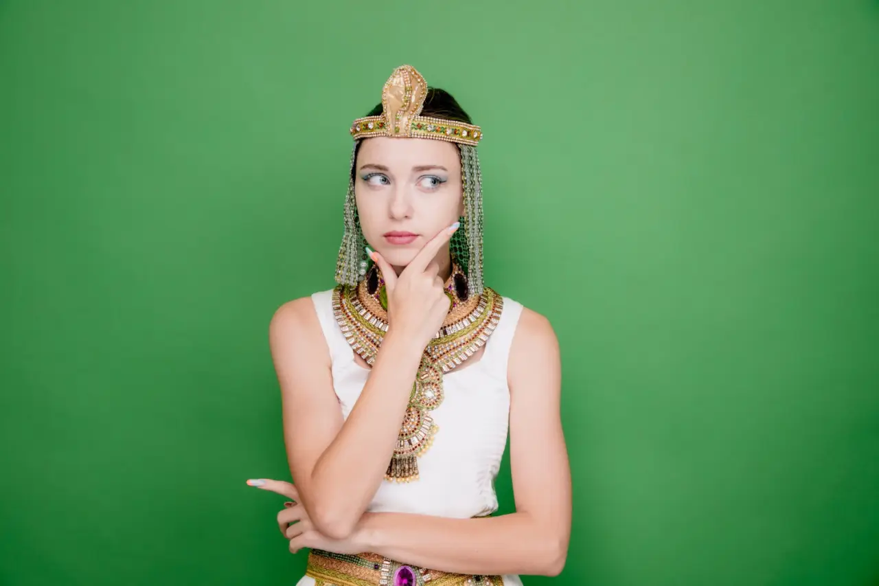 8 Fascinating Artifacts Linked To The Life Of Queen Cleopatra 4 A woman dressed in a Cleopatra-style costume poses thoughtfully against a green background.