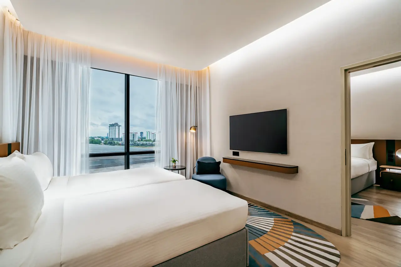 Novotel Johor Bahru City Centre Opens 21 Modern hotel family room with twin beds, large window overlooking Johor Bahru, and adjoining bedroom.