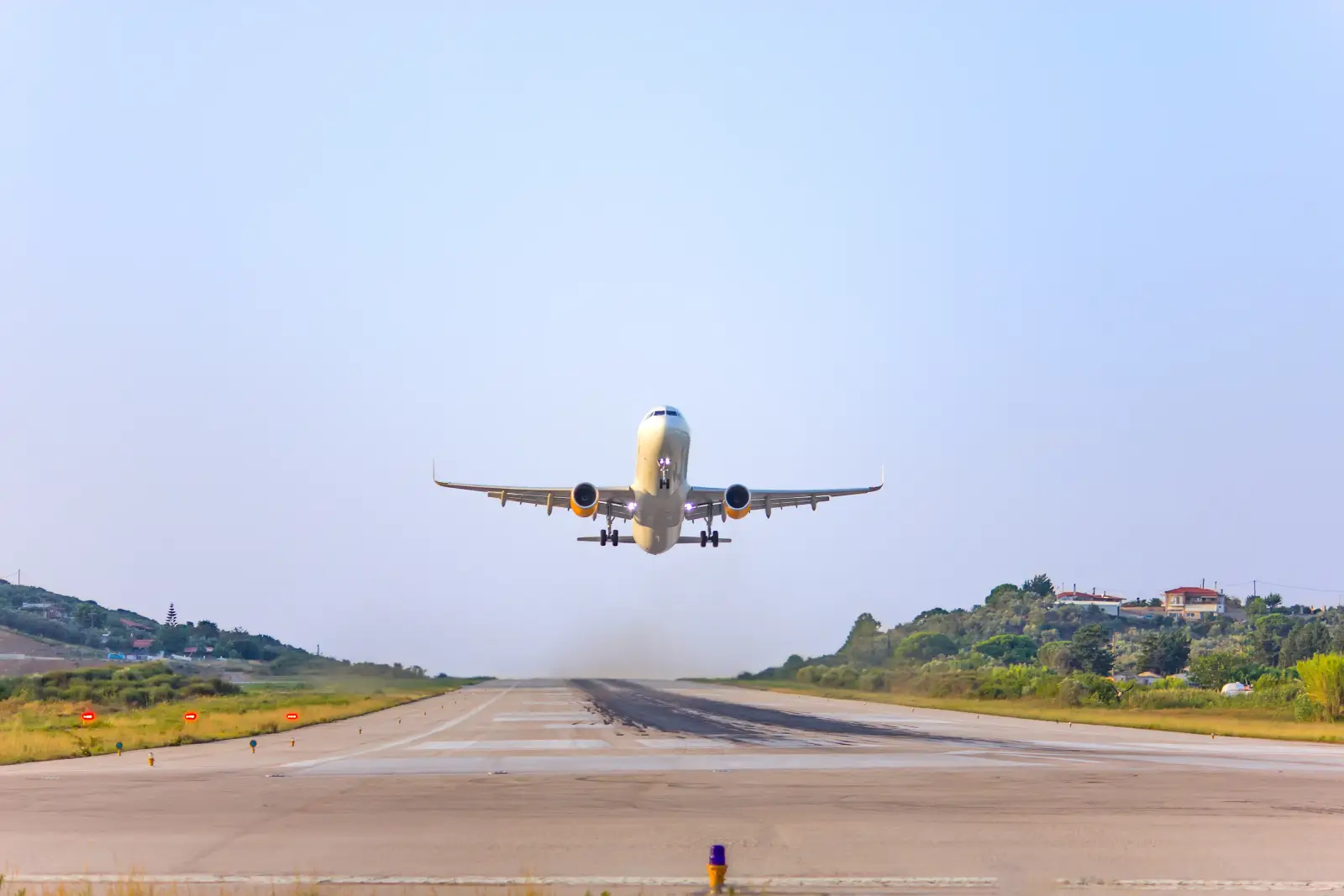 Commercial airplane taking off from a small runway with hills and houses in the background.