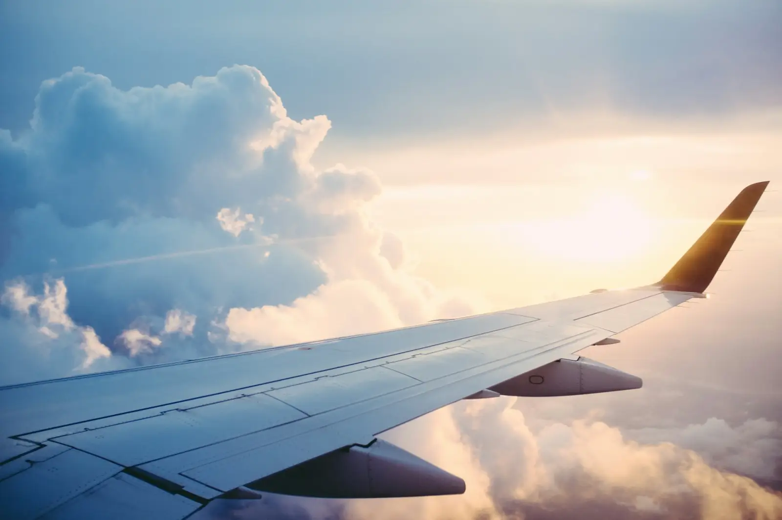Airplane wing flying above clouds during a commercial flight at sunset