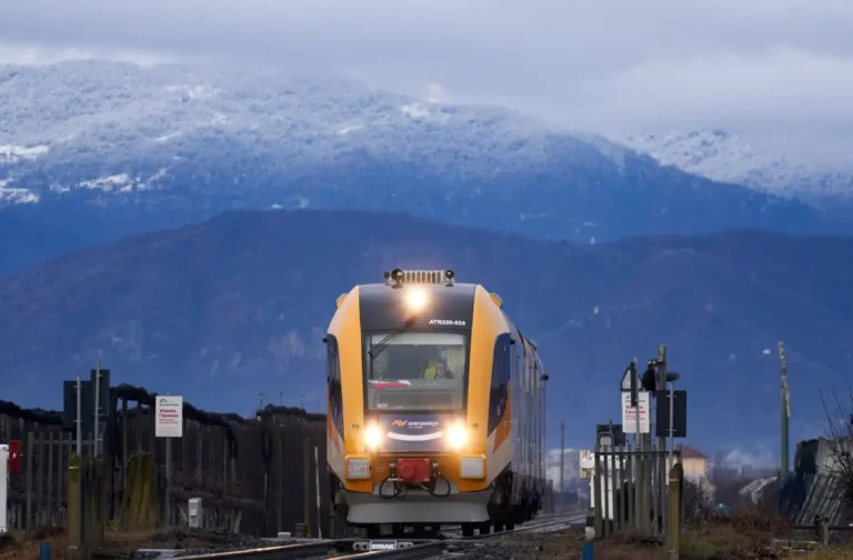 Arenaways train traveling on a rural track with snow-covered mountains in the background.