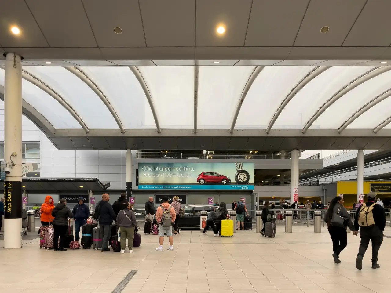 Holiday travelers with suitcases exiting Gatwick Airport terminal in Sussex, England