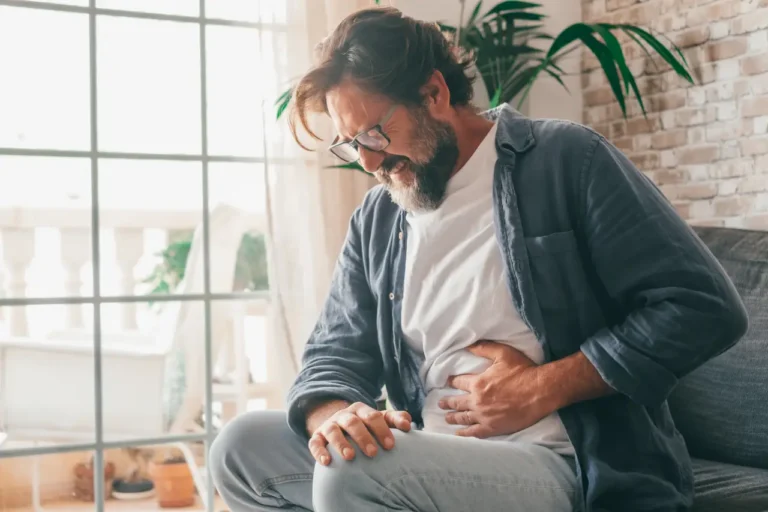 Middle-aged man sitting on a sofa holding his stomach in pain at home