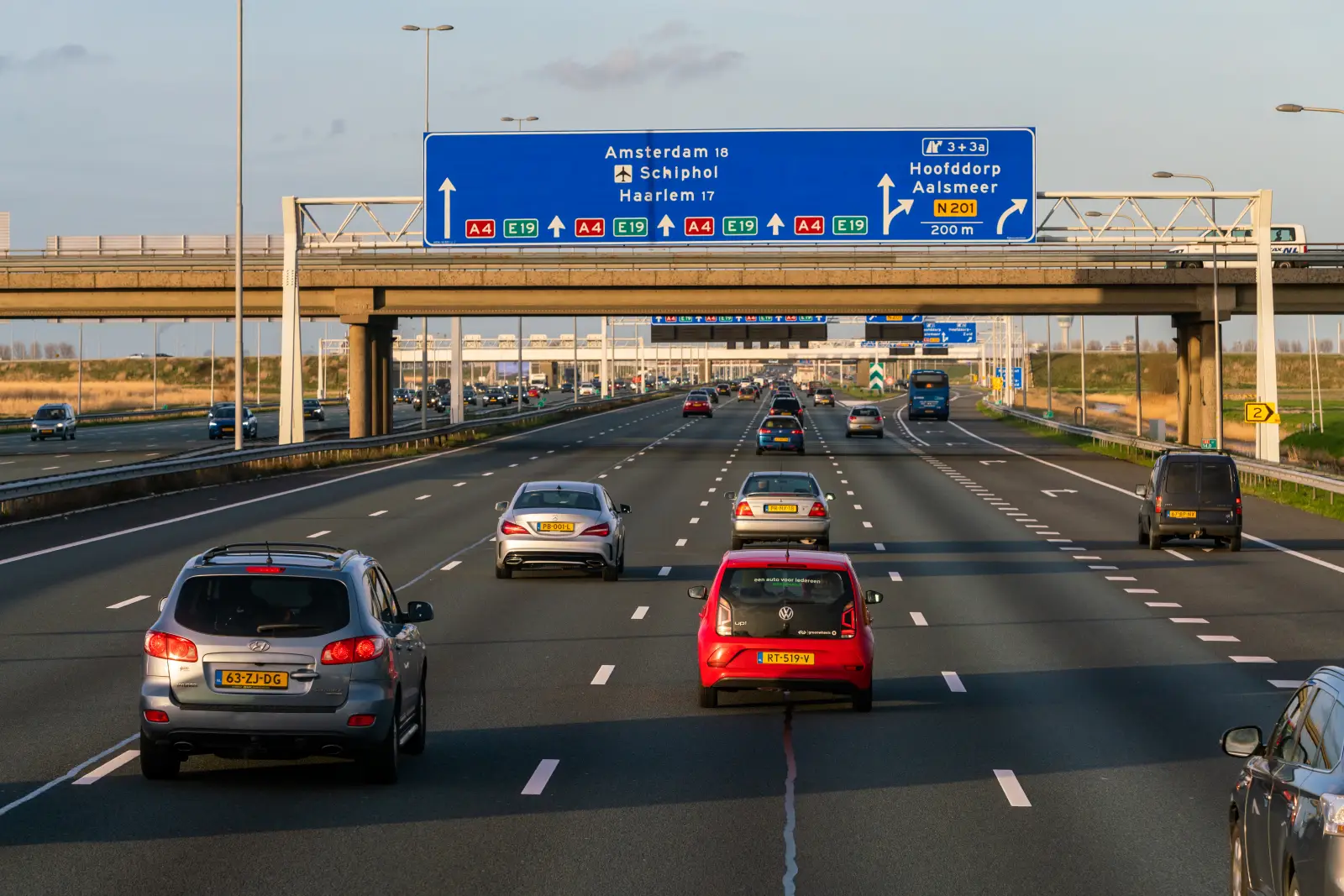 Cars driving on a Dutch motorway with overhead road signs pointing to Amsterdam, Schiphol and Haarlem