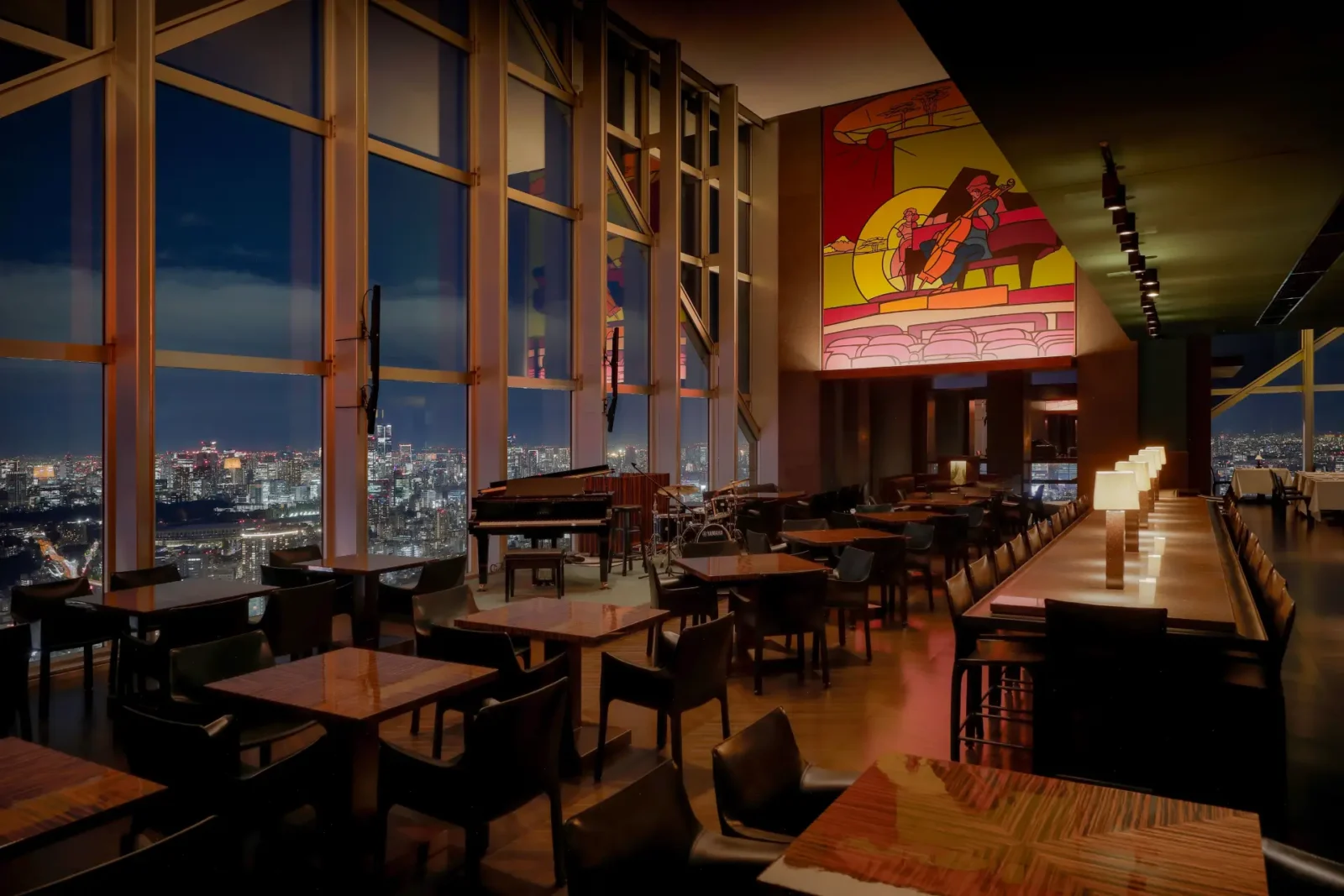 Interior of New York Bar at Park Hyatt Tokyo with floor-to-ceiling windows, city skyline views and illuminated bar seating at night.