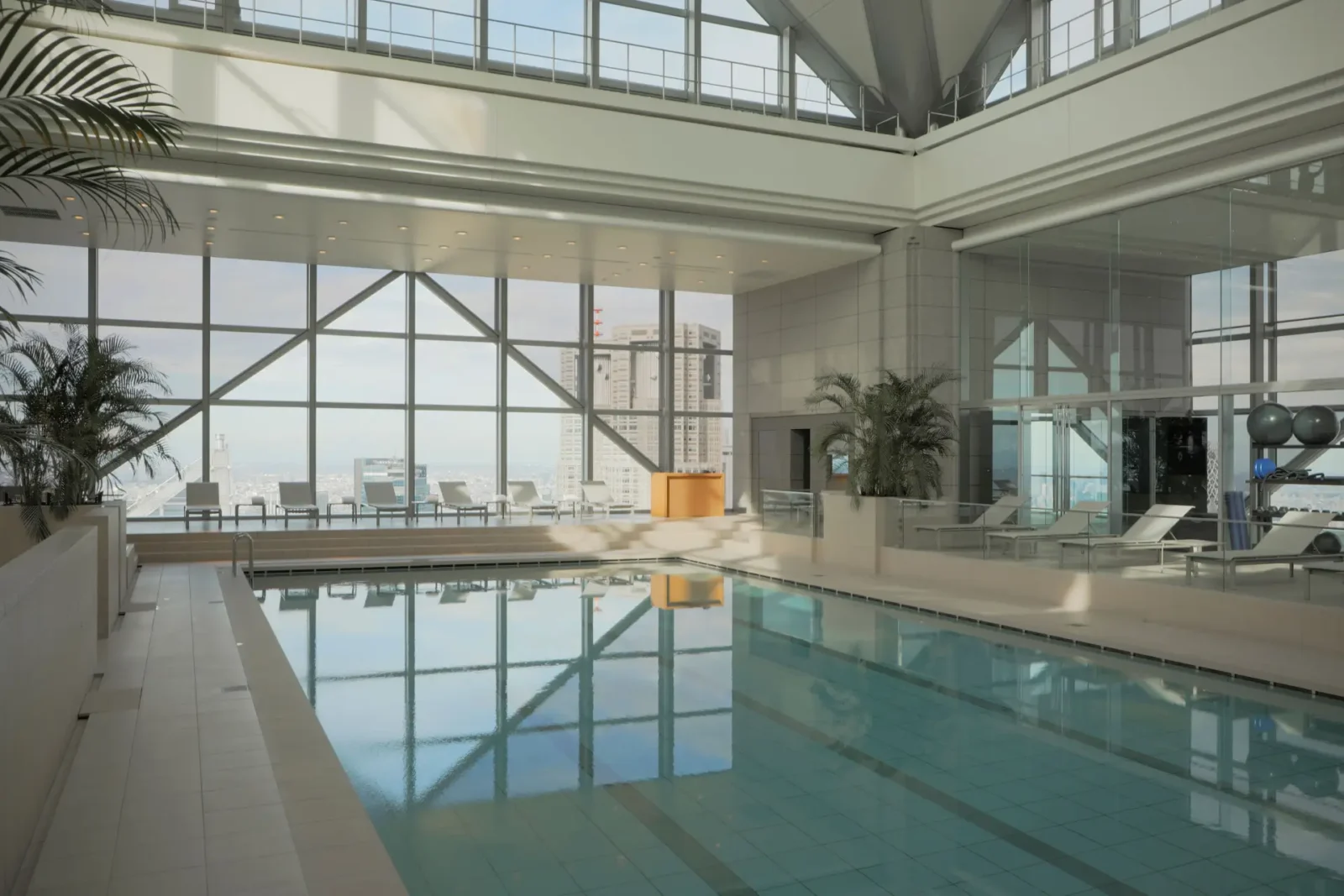 Indoor swimming pool at Park Hyatt Tokyo with floor-to-ceiling windows and panoramic city views in daylight.