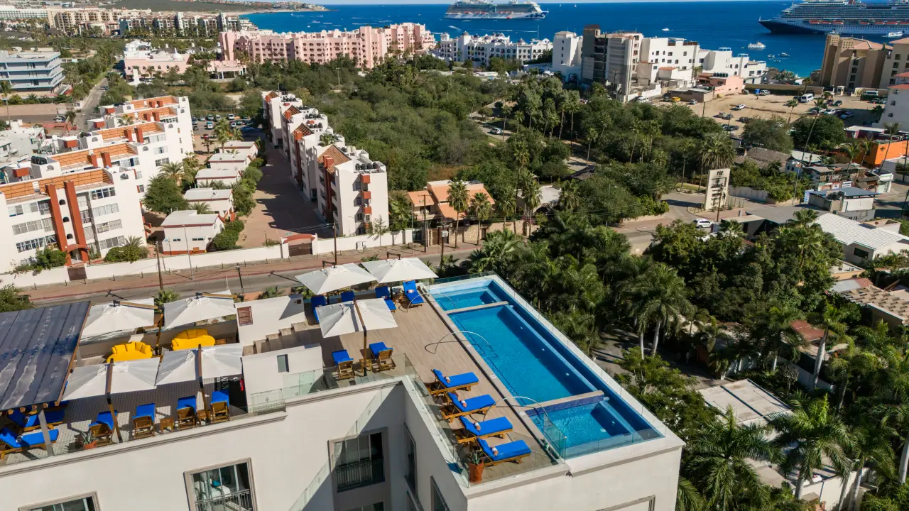 Rooftop swimming pool with sun loungers overlooking a coastal city and cruise ships at sea.