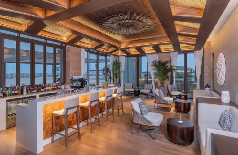 Luxury resort bar interior at Anantara Mina Ras Al Khaimah Resort with modern seating, illuminated counter, and floor-to-ceiling windows.