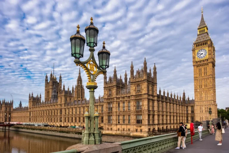 Tours 19 Tourists walk across Westminster Bridge with Big Ben and the Houses of Parliament in London under a cloudy sky.