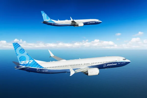 Two Boeing 737 MAX aircraft fly in formation over the ocean under a clear blue sky.