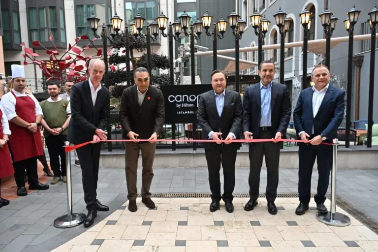 News From Turkey - Türkiye 15 Hilton executives cut a red ribbon during the opening ceremony of Canopy by Hilton Istanbul Taksim, with hotel staff and the property courtyard visible behind them.