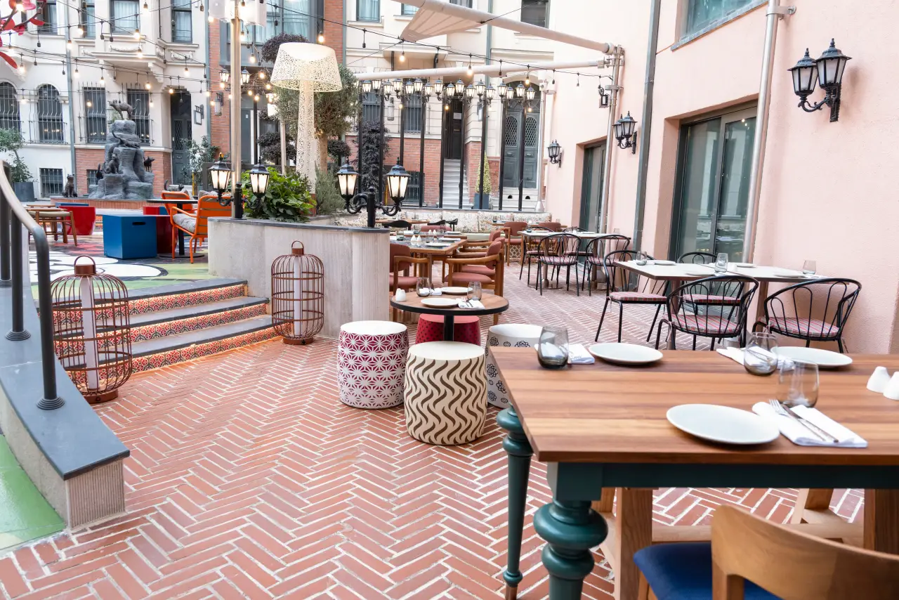 Hilton Opens Canopy By Hilton Istanbul Taksim 5 An open-air courtyard dining area at Canopy by Hilton Istanbul Taksim with outdoor tables, decorative lighting, brick flooring, and colourful seating surrounded by restored historic façades.