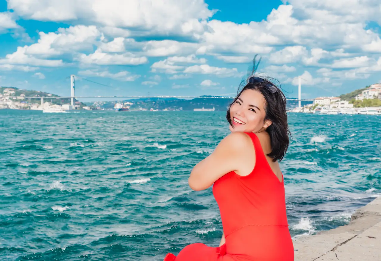 Turkey Opens Its Doors To Chinese Travellers With New Visa-Free Travel 7 Smiling Chinese woman in a red dress sitting by the Bosphorus in Istanbul, with the bridge and sea behind her