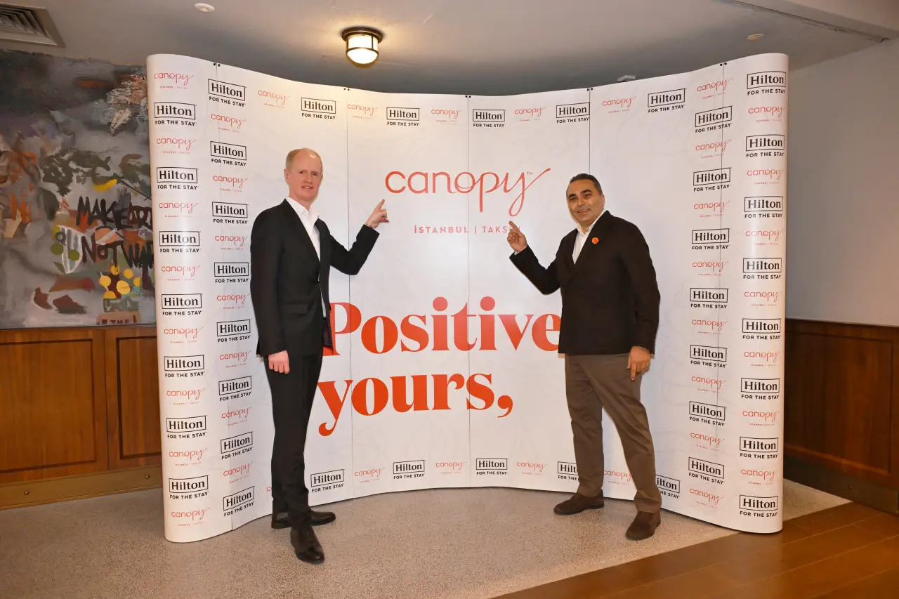 Hilton Opens Canopy By Hilton Istanbul Taksim 4 David Kelly stands on the left and Can Özmeriç stands on the right in front of a Canopy by Hilton Istanbul Taksim branded backdrop during the hotel’s opening event, pointing toward the logo and slogan.
