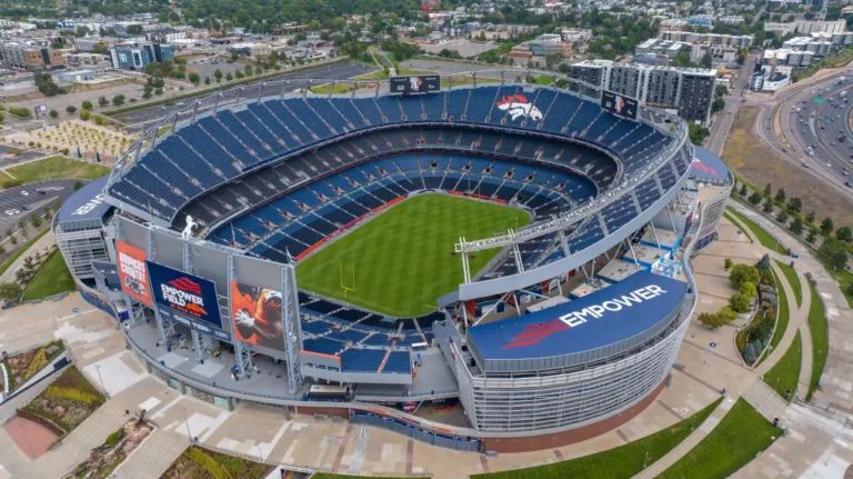 Aerial view of Empower Field at Mile High in Denver, showing the empty NFL stadium surrounded by city streets and nearby neighborhoods.