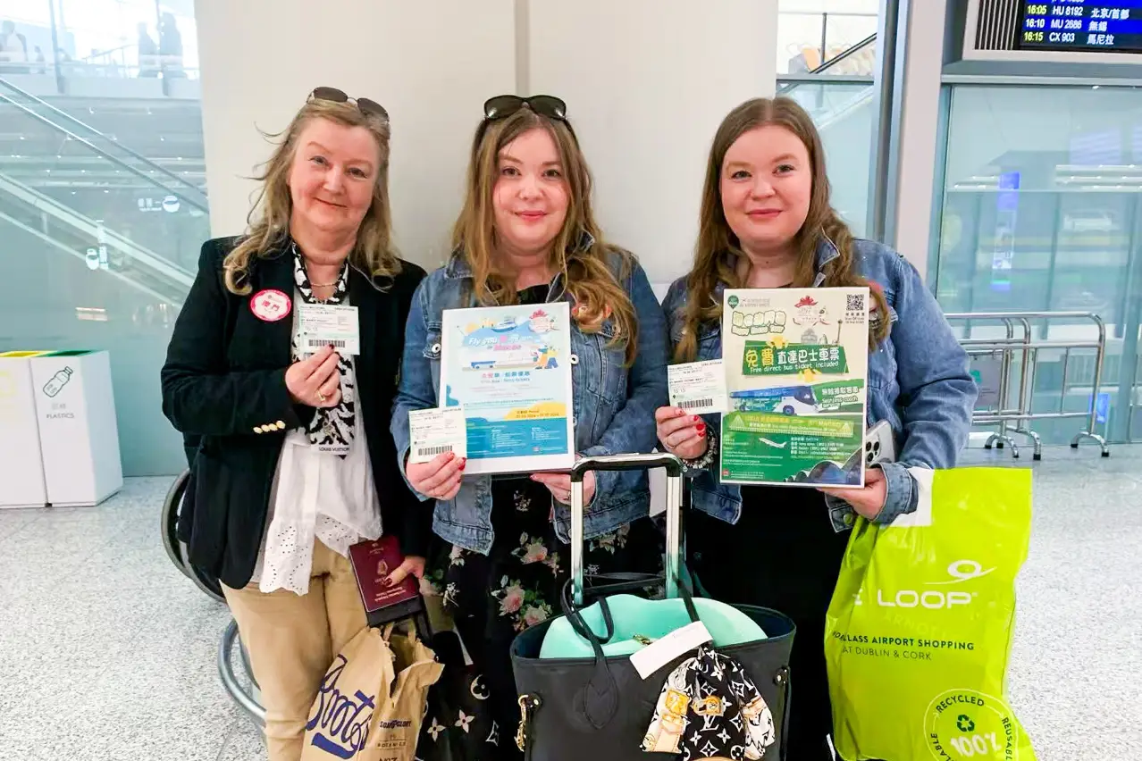 Macao Offers Free Bus Transfers For International Visitors From Hong Kong International Airport 3 Three international travellers hold free coach tickets and promotional leaflets at an airport terminal, preparing for a direct bus transfer to Macao.