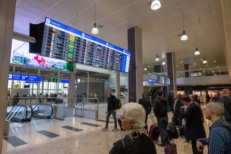 Passengers standing in the terminal checking the arrivals and departures boards at Geneva Airport in Switzerland