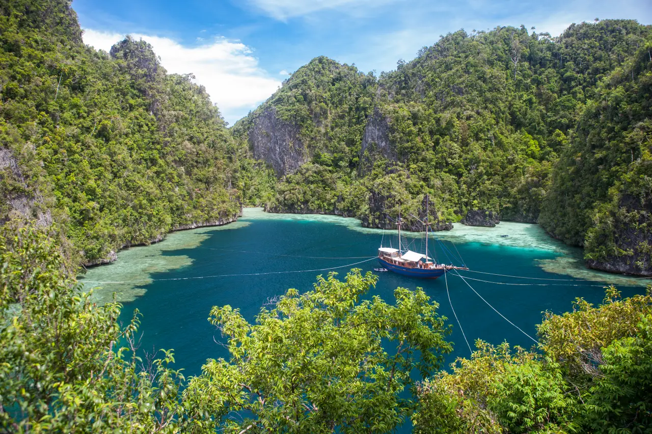 Small boat anchored in a turquoise lagoon surrounded by limestone islands in Misool, Raja Ampat, Indonesia.