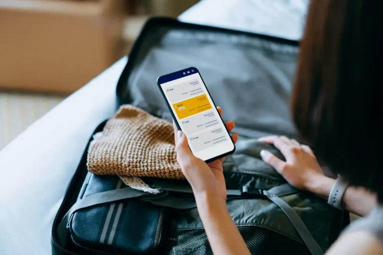 Technology 20 Traveler holding a smartphone showing a flight booking app while packing a suitcase.