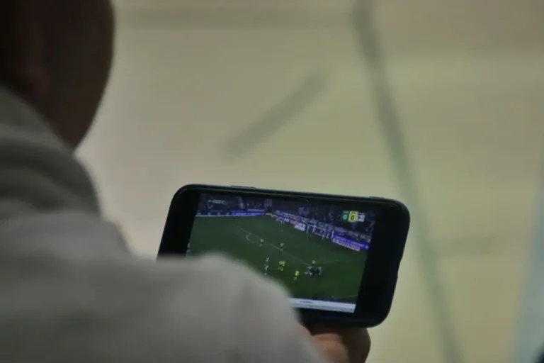 Person watching a live soccer match on a smartphone screen in an indoor setting.
