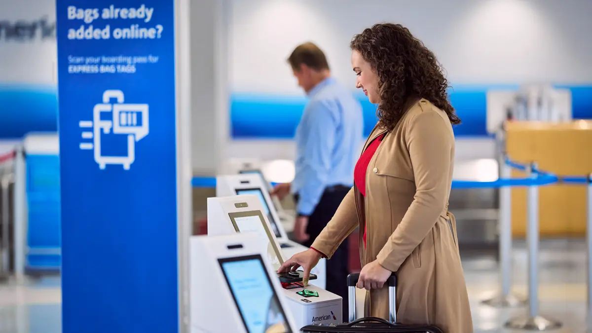 Passenger uses self-service kiosk to print baggage tag at American Airlines airport check-in area