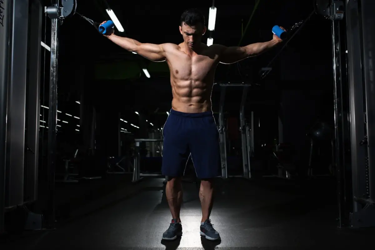 Muscular man performing cable chest fly exercise in a dark gym, showing defined abs and upper body strength