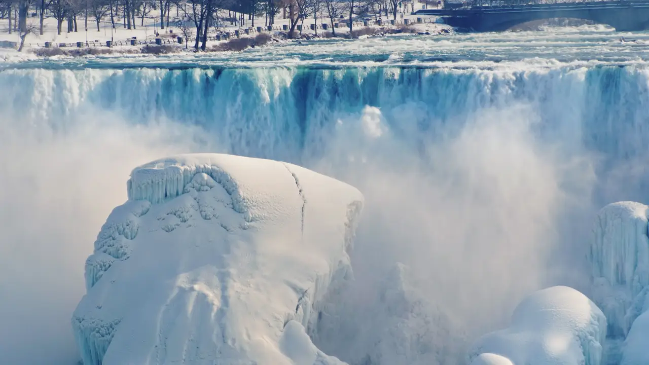 Partially frozen Niagara Falls with water cascading over ice-covered cliffs in winter on the American side