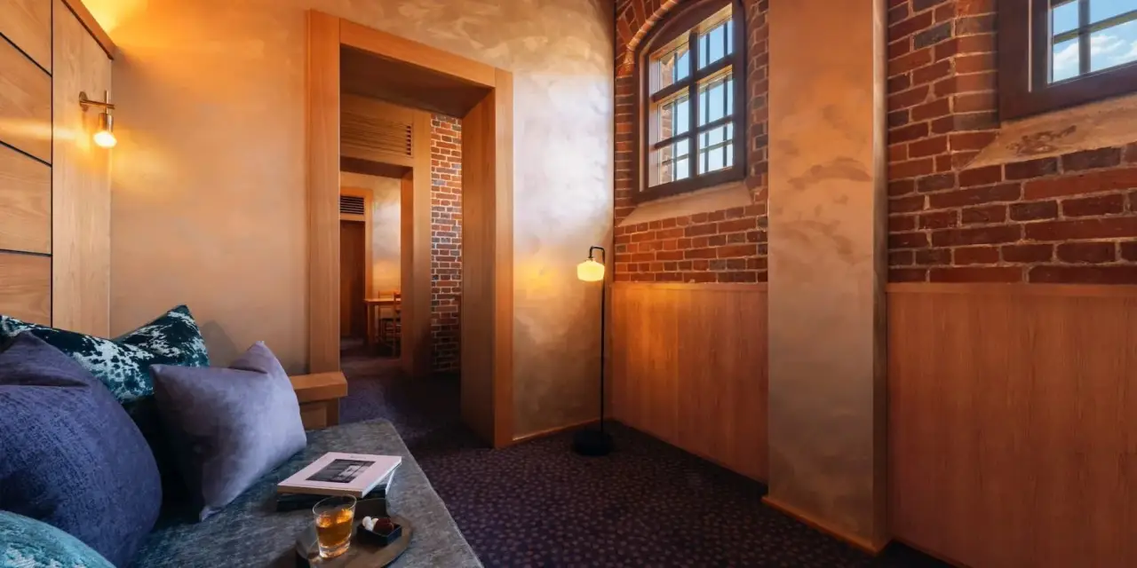 Japan’s First Luxury Hotel Housed In A Former Prison Will Open In June 5 Living area at HOSHINOYA Nara Prison featuring exposed red brick walls, wood paneling and warm ambient lighting