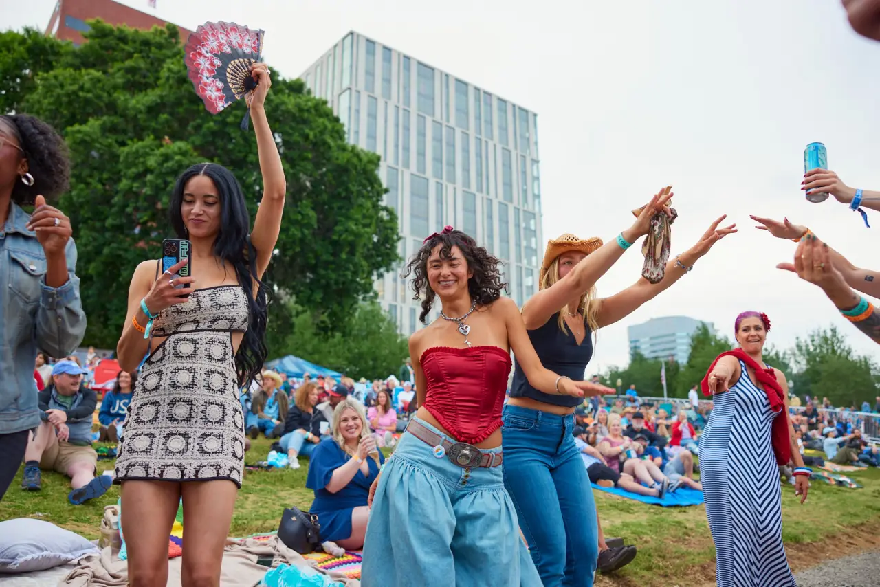 Festivalgoers dance and celebrate during Portland’s Waterfront Blues Festival at Tom McCall Waterfront Park with crowds and city skyline behind