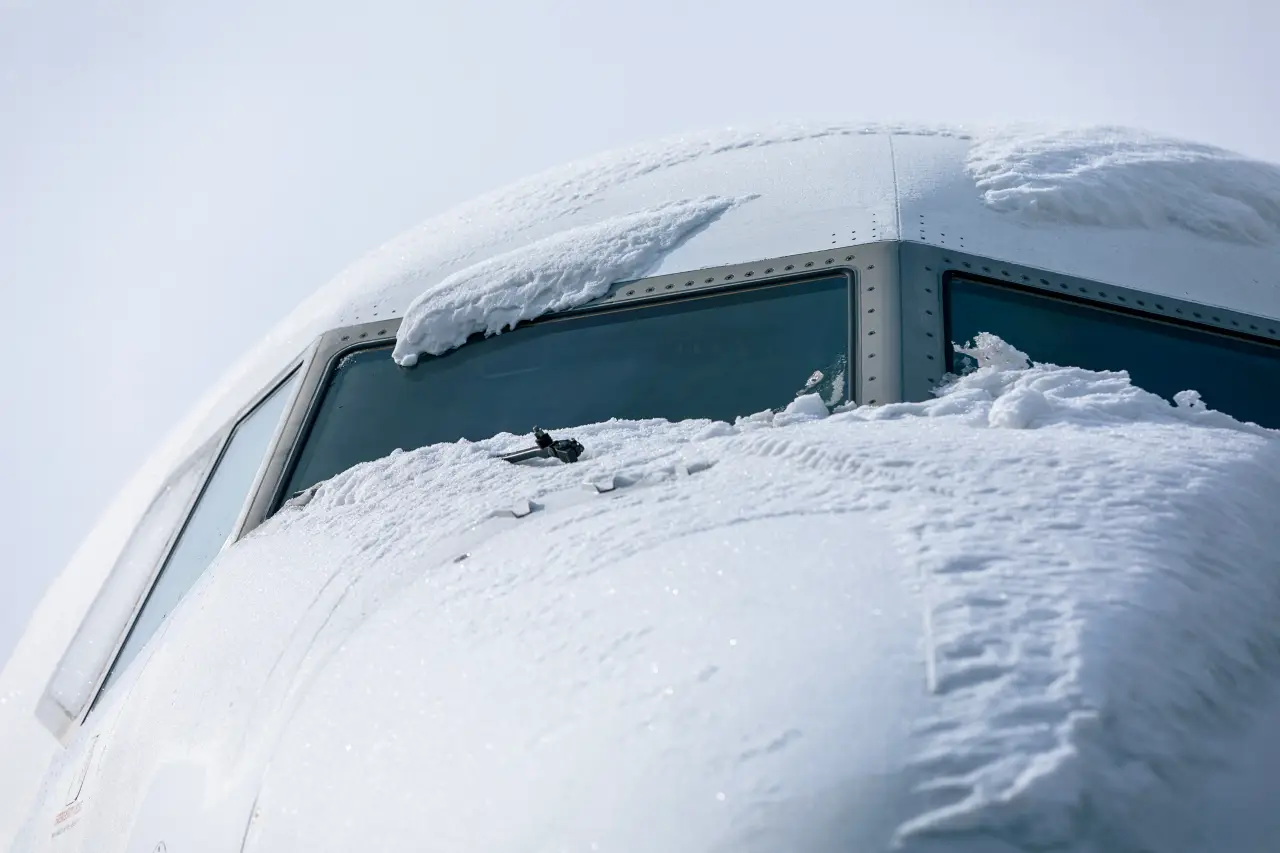 Snow-covered cockpit windows of a passenger airplane awaiting de-icing during a winter storm at an airport.