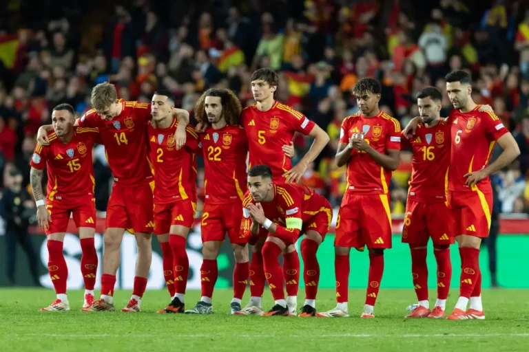 Sports Tourism 19 Spain national football team players line up on the pitch before kickoff, wearing red home kits with yellow details.