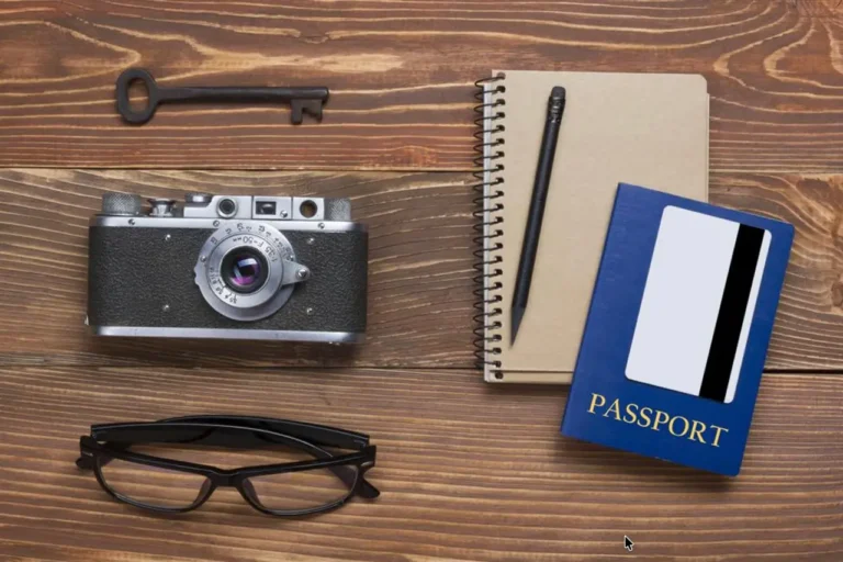 Technology 18 Flat lay of a travel desk with a vintage camera, passport, notebook, pen, glasses, and key on a wooden table.
