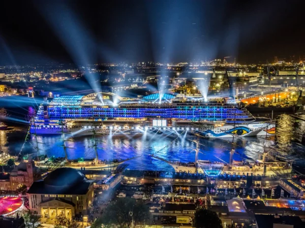 Home 6 AIDA cruise ship illuminated at night in port with city skyline and lights during large-scale cruise event
