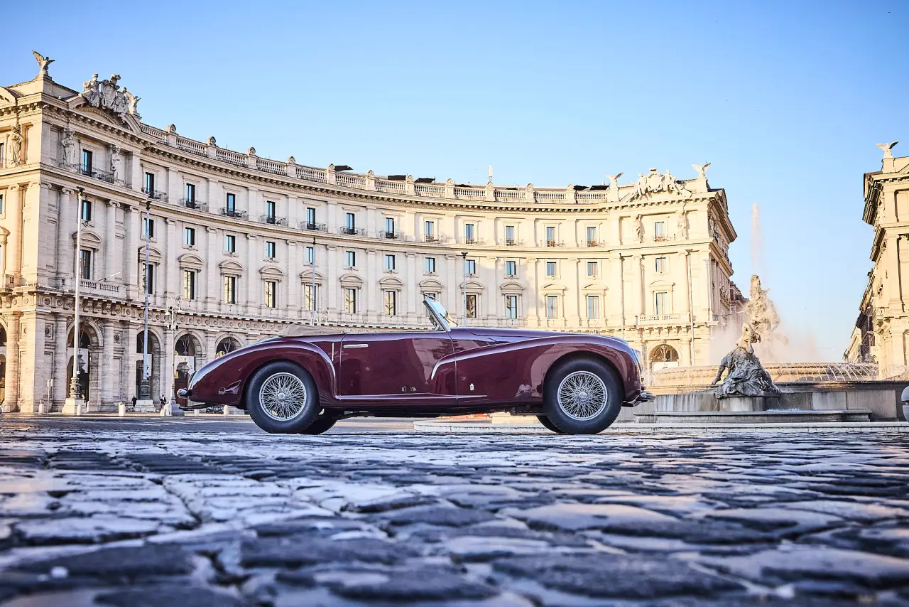 Historic Italian convertible car displayed in Rome city square with classical architecture during Anantara Concorso Roma event