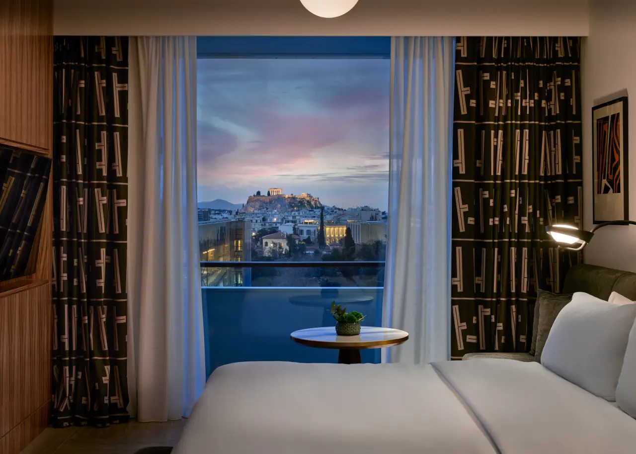 Luxury hotel bedroom with balcony view of the Acropolis in Athens at sunset, featuring modern decor and soft lighting