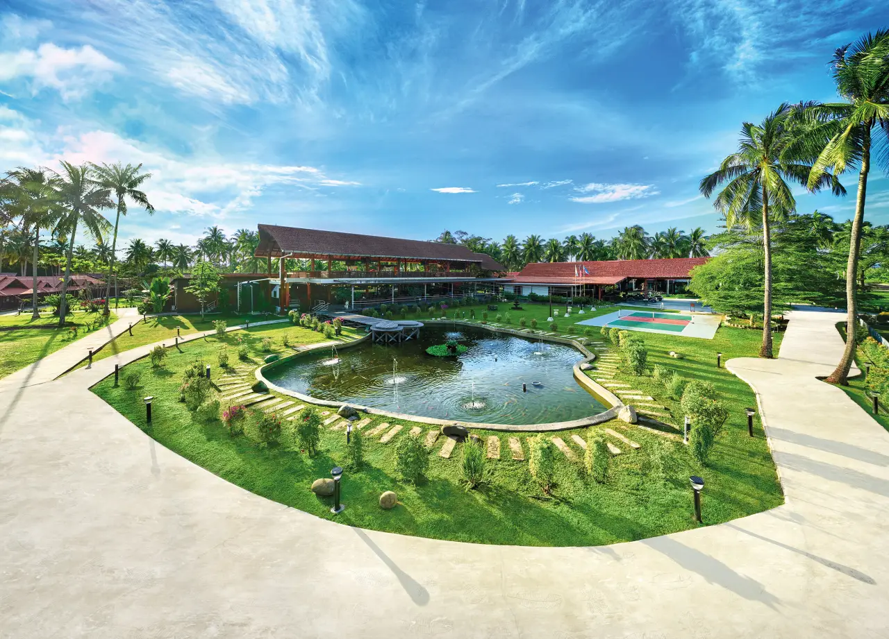 Tropical beachfront hotel in Sabah with landscaped gardens, pond, and palm trees under a bright blue sky