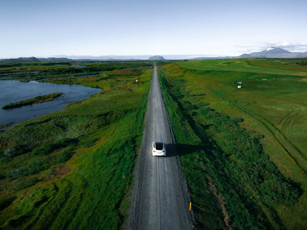 Electric car driving along Iceland Ring Road through green landscapes and lakes under clear skies