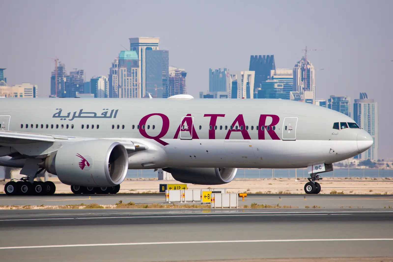 Qatar Airways aircraft on runway at Doha airport with city skyline in the background