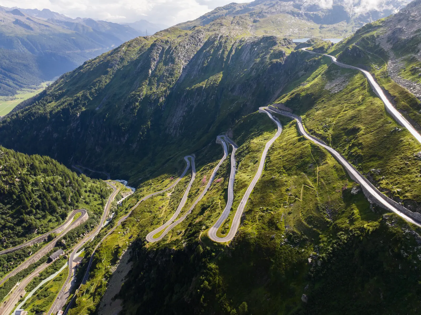 Winding alpine mountain road with sharp hairpin bends in Switzerland, surrounded by green valleys and steep rocky slopes