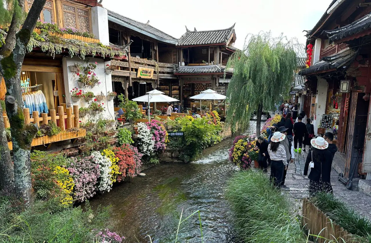 Traditional Chinese water town street with canal, wooden houses, flowers and tourists walking along the riverside market