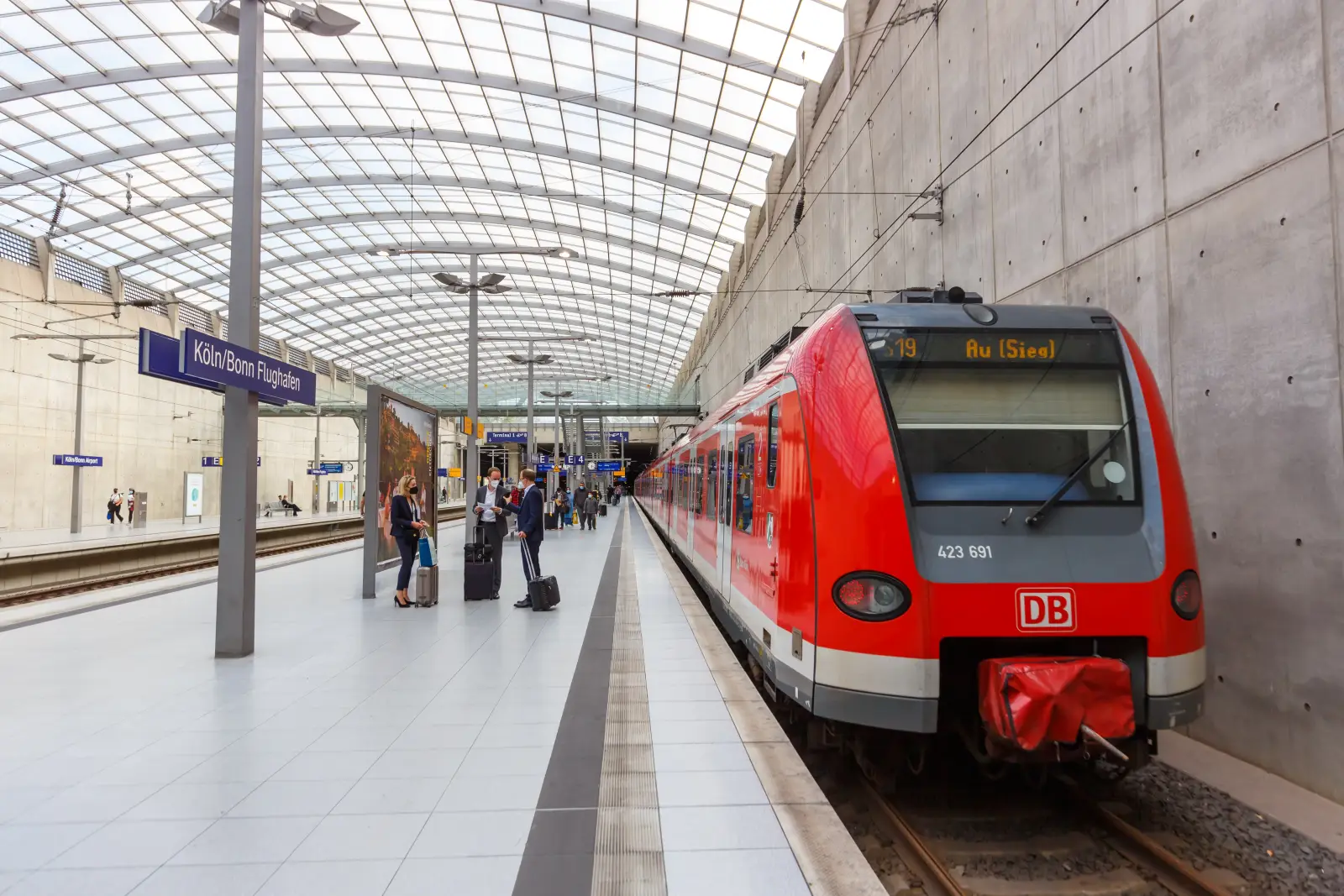 Red Deutsche Bahn S-Bahn train at Köln/Bonn Airport station platform with passengers and luggage