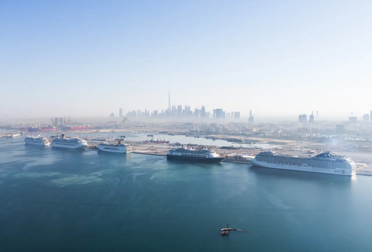 Multiple cruise ships docked at Dubai’s Port Rashid cruise terminal with the Dubai skyline and Burj Khalifa in the distance.