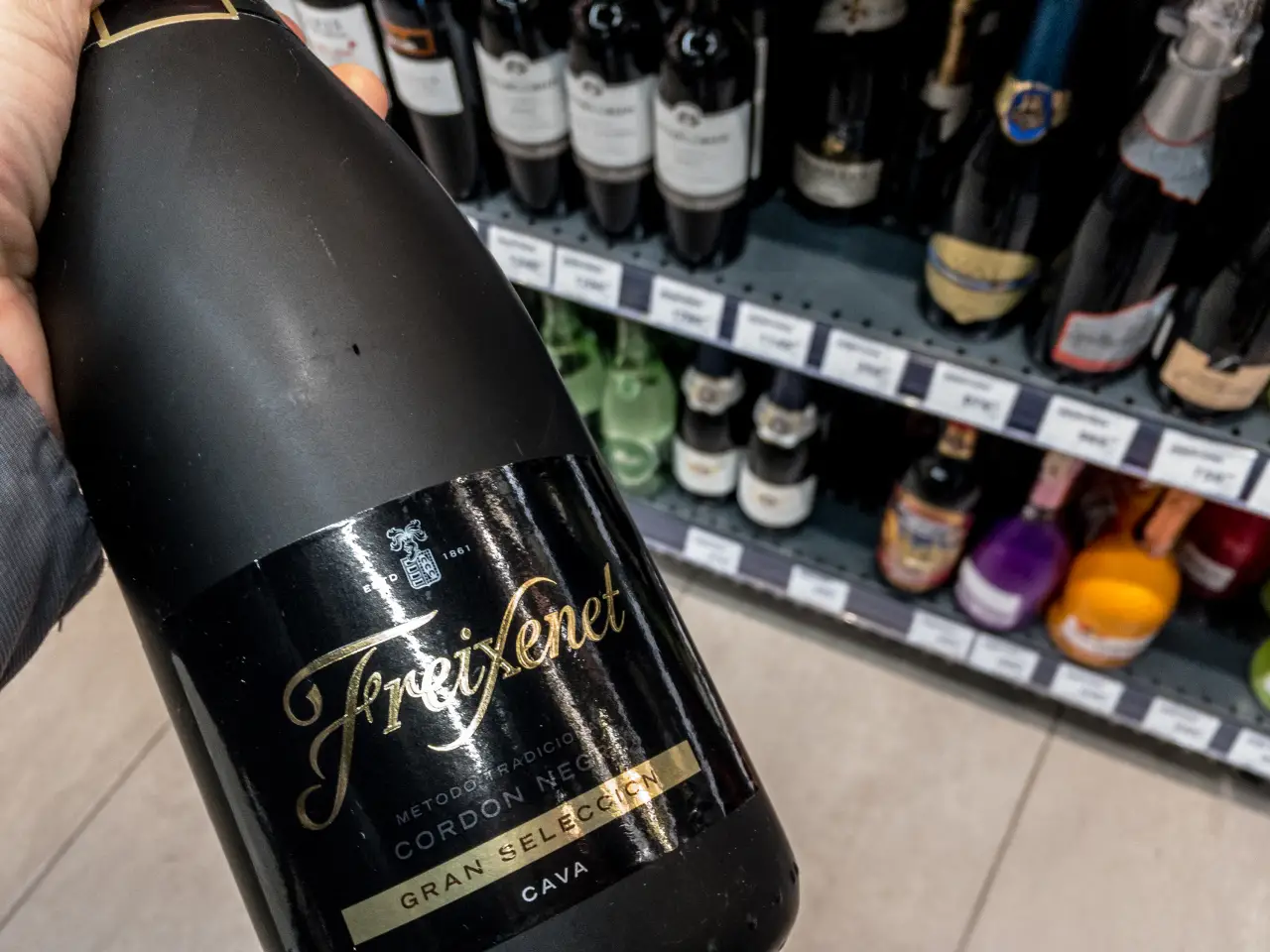 Freixenet Cordon Negro cava bottle held in a store wine aisle with sparkling wine bottles on shelves