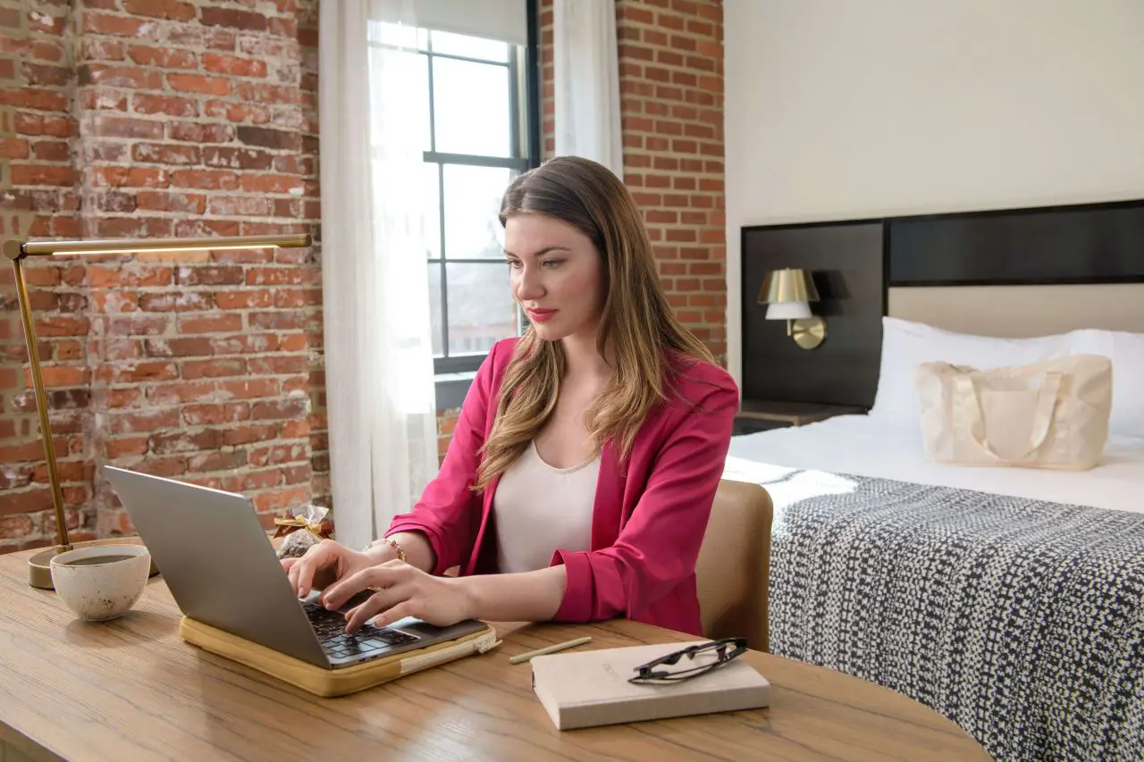 Woman using laptop in a modern hotel room while planning a stay with Hilton AI Planner