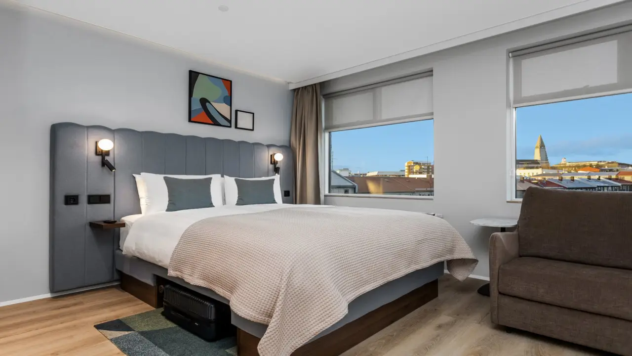 Modern hotel room in Europe with large bed, city views through windows and contemporary interior design