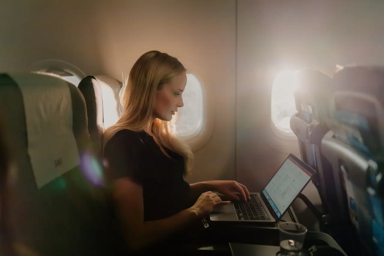 Passenger using a laptop on an airplane seat with sunlight through the window, illustrating inflight WiFi connectivity