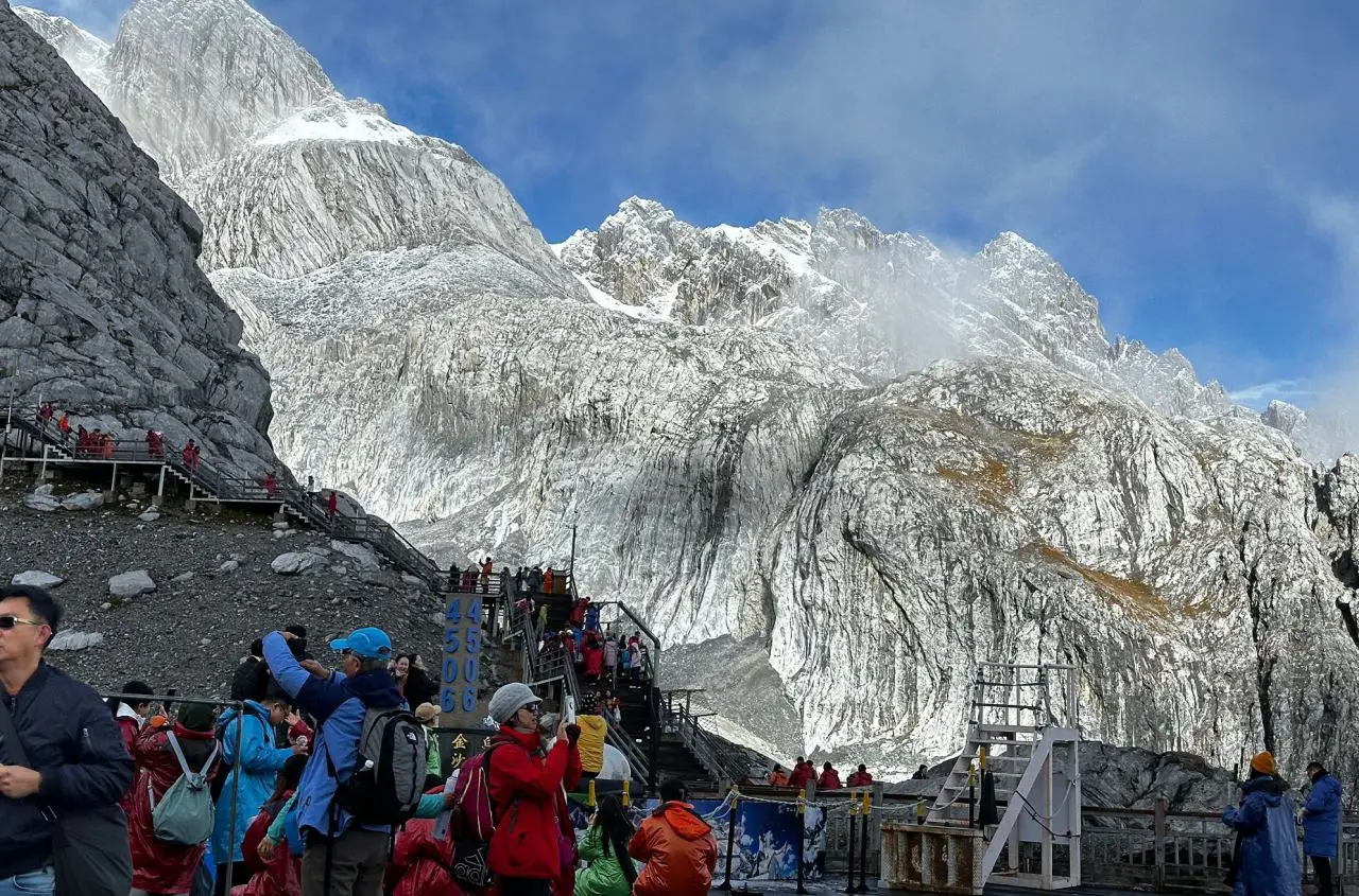 Tourists visiting Jade Dragon Snow Mountain viewpoint near Shangri-La in Yunnan, China with dramatic snowy peaks and observation stairs